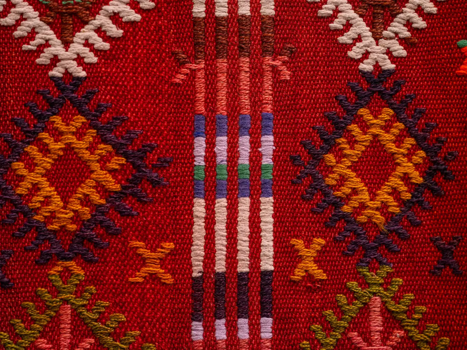 Kırmızı zeminli, turuncu ve mor motifli el dokuması kilim dokusu, yakın çekim